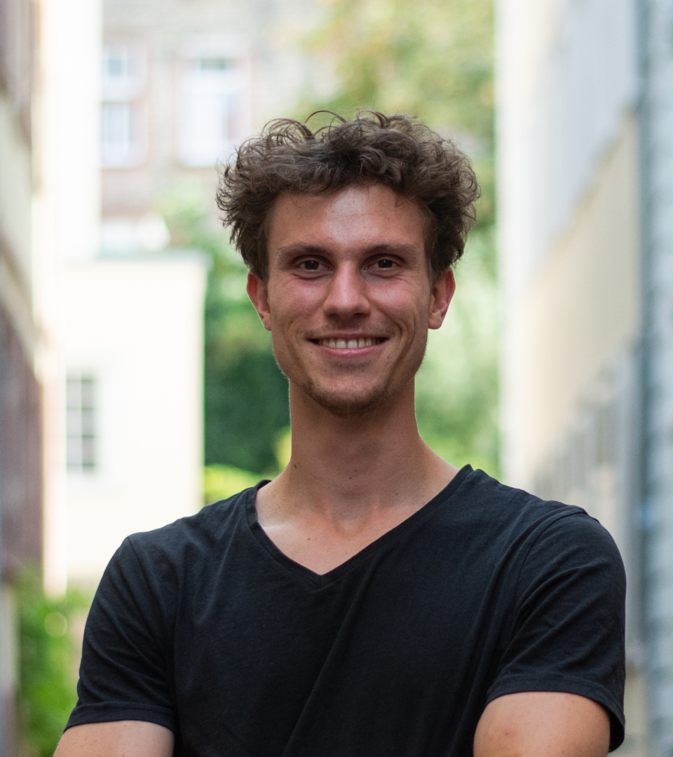 Porträt von Philipp, lächelnd in einem schwarzen T-Shirt, vor einem unscharfen hellen Hintergrund